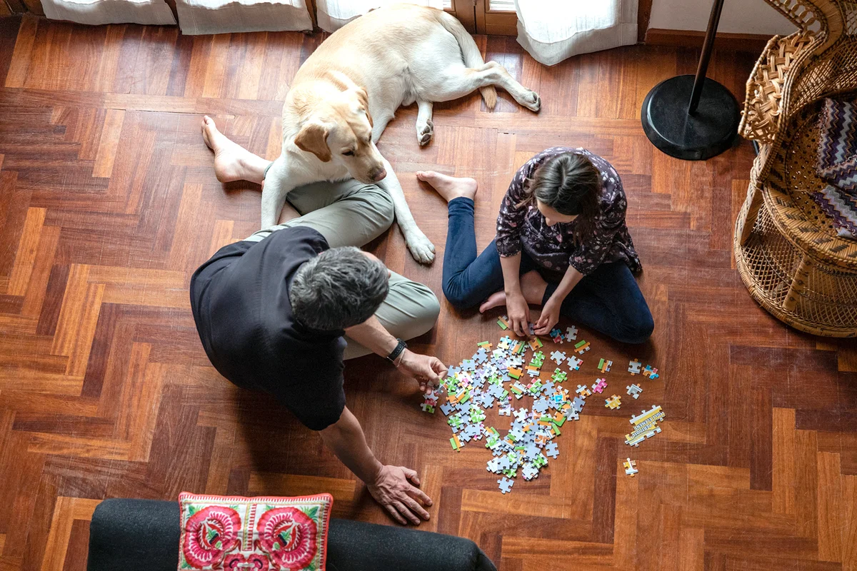 Father and daughter sitting on living room floor, doing jigsaw puzzle