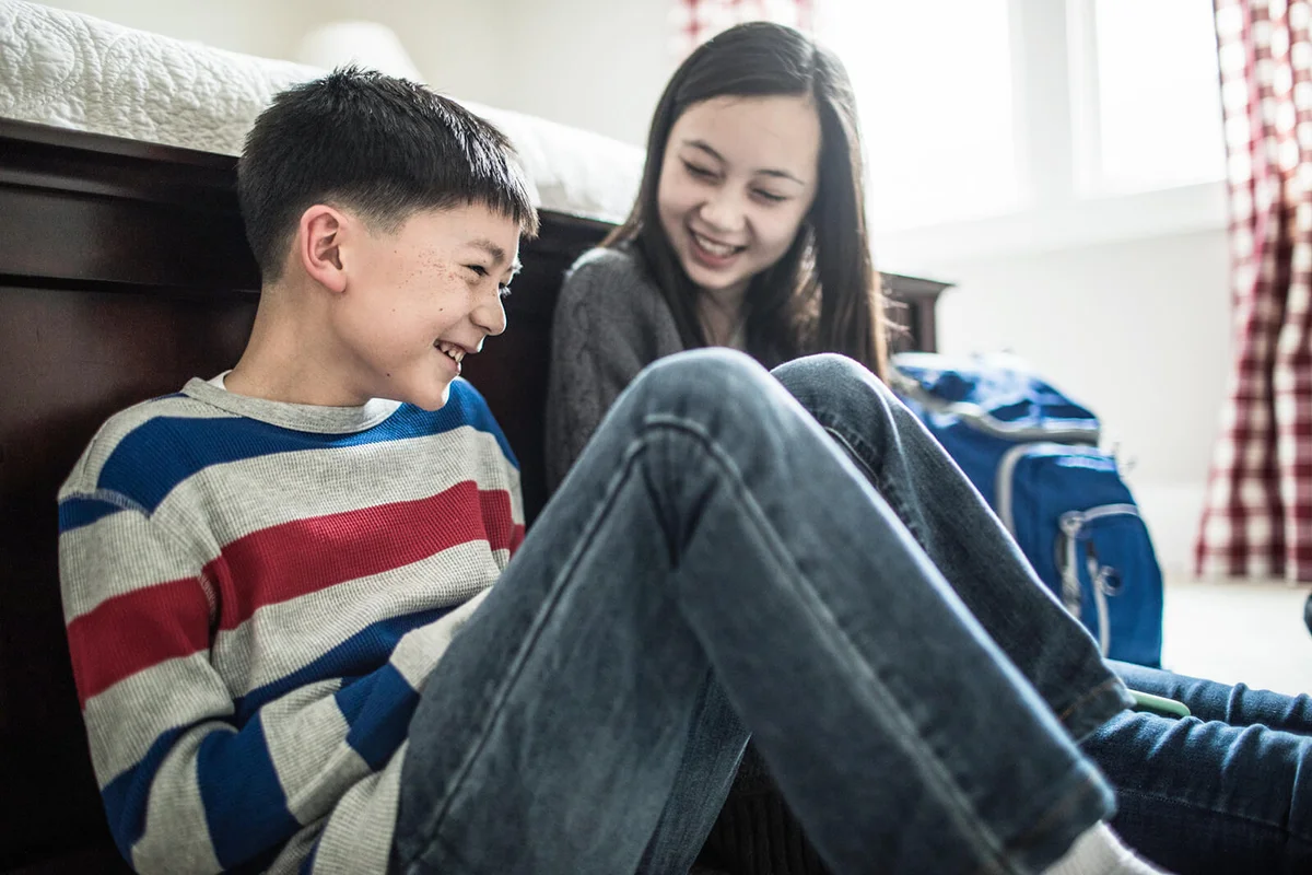 Brother and sister laughing in bedroom at home