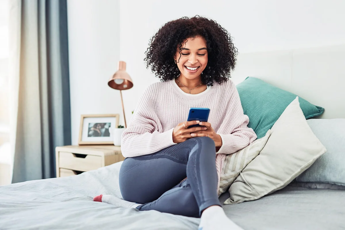 young woman sitting on her bed and using her cellphone