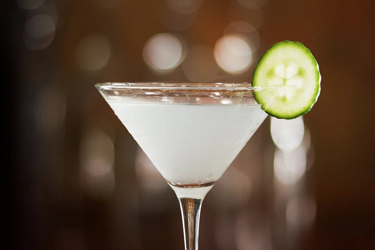 cucumber martini served on a bar top garnished with a cucumber slice