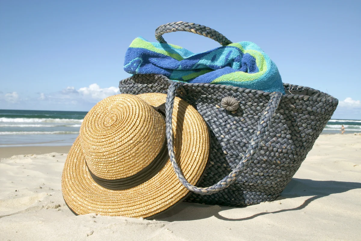 Straw hat lies on white-sand beach beside blue straw bag