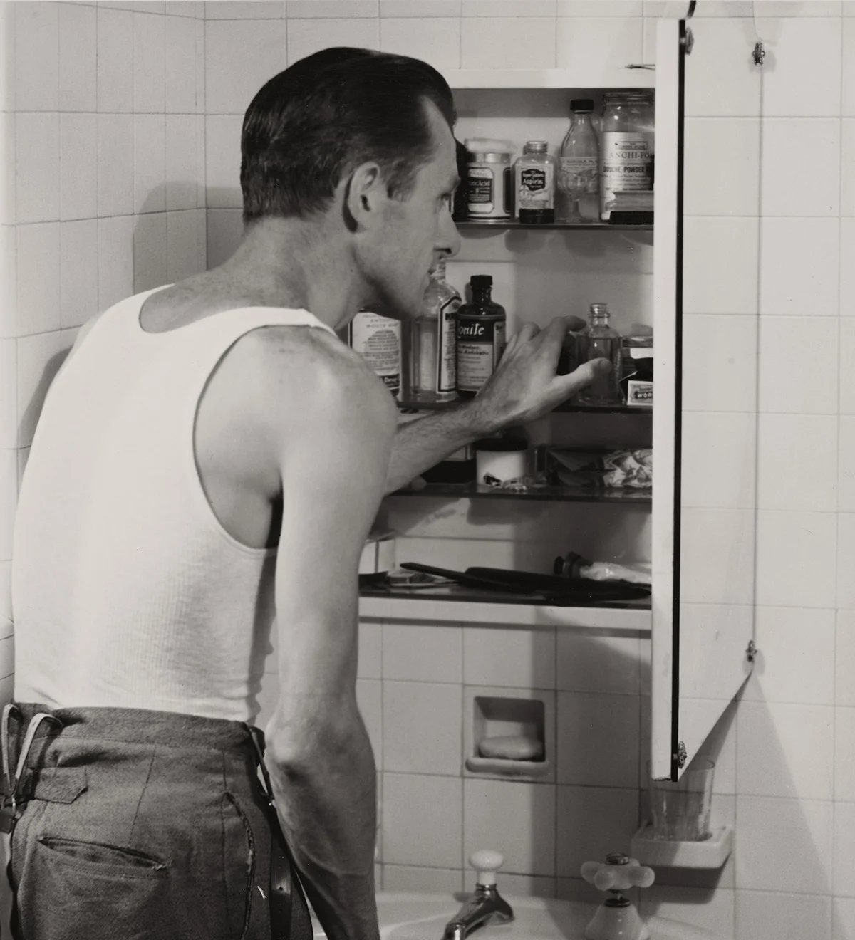 A man looks through his medicine cabinet in the bathroom, circa 1955