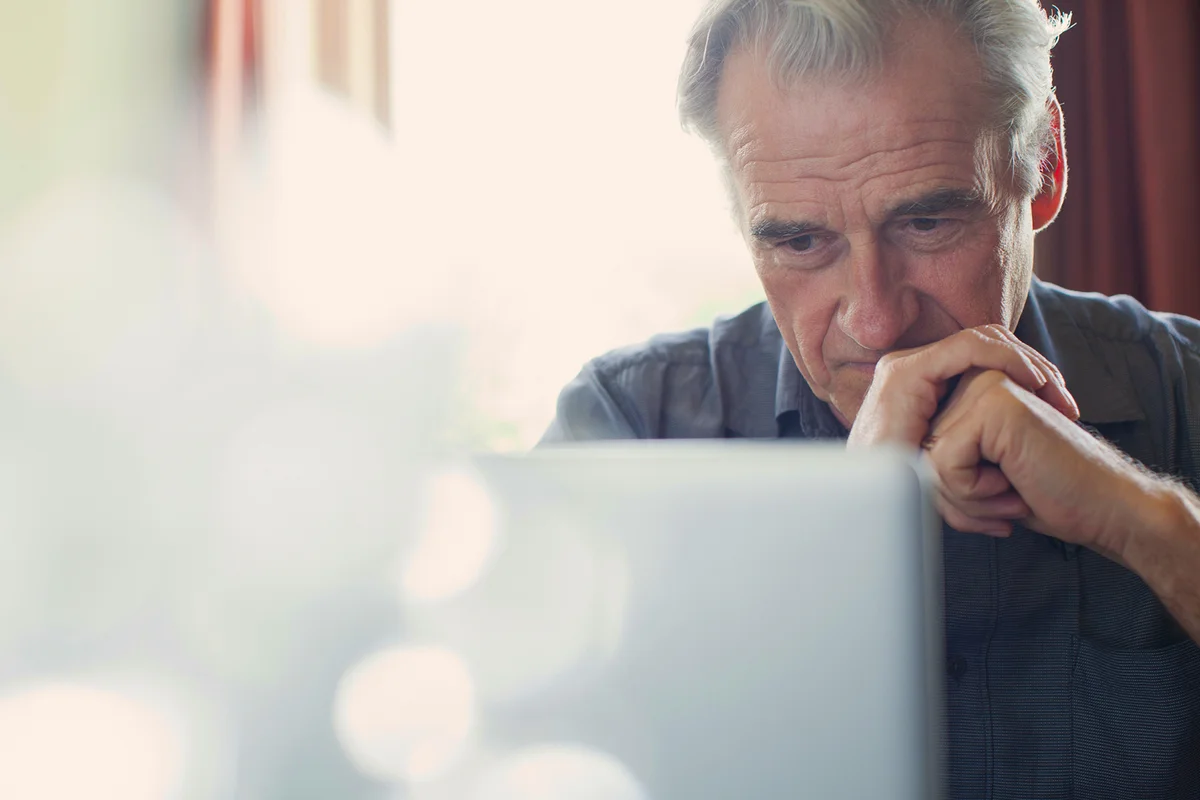 Senior man with hands clasped using laptop