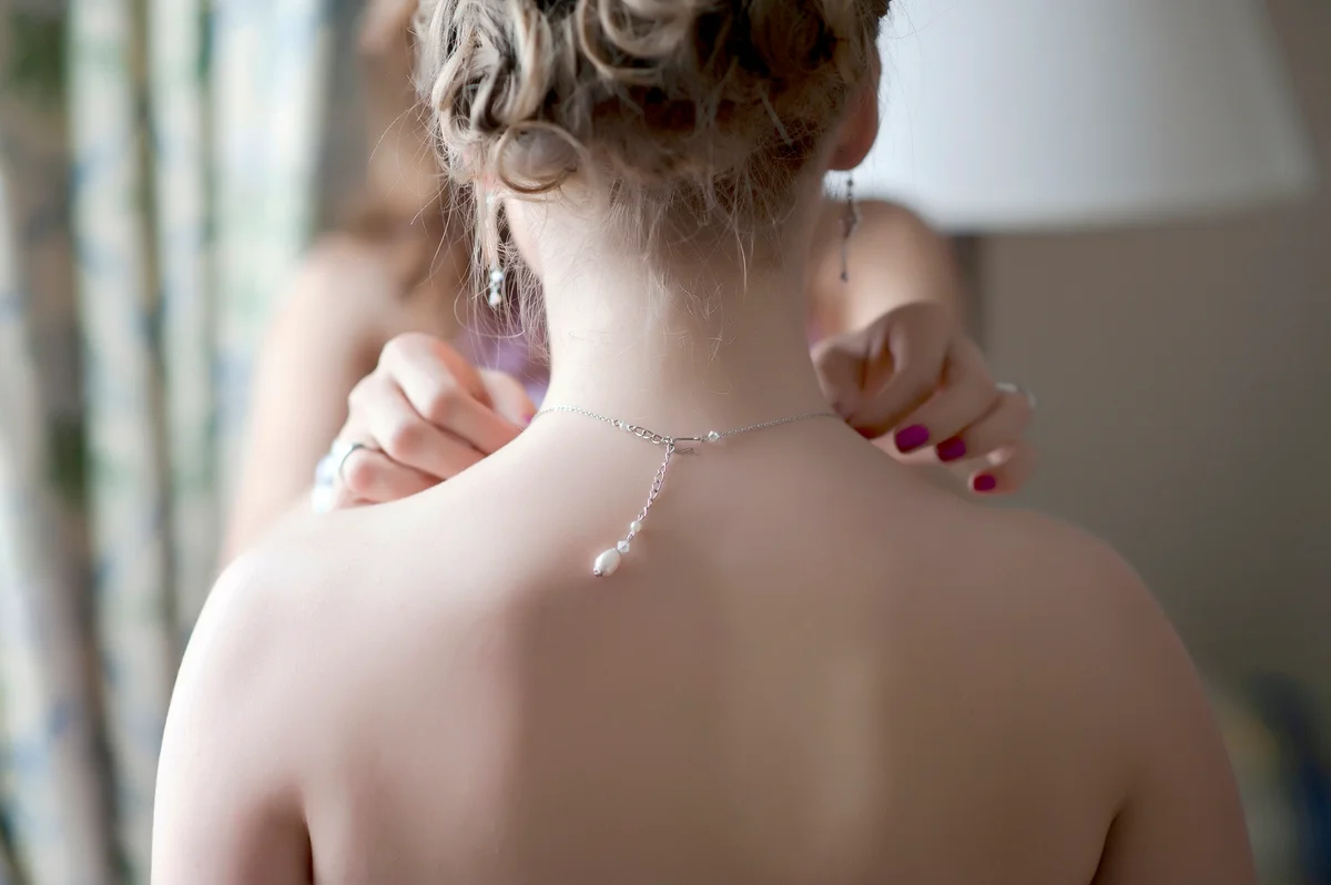 Bridesmaid fixing necklace on bride