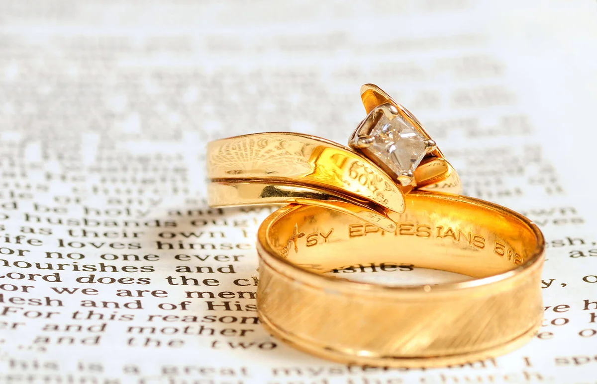 Two gold wedding rings rest on the marriage passage from Ephesians 5 in the Bible