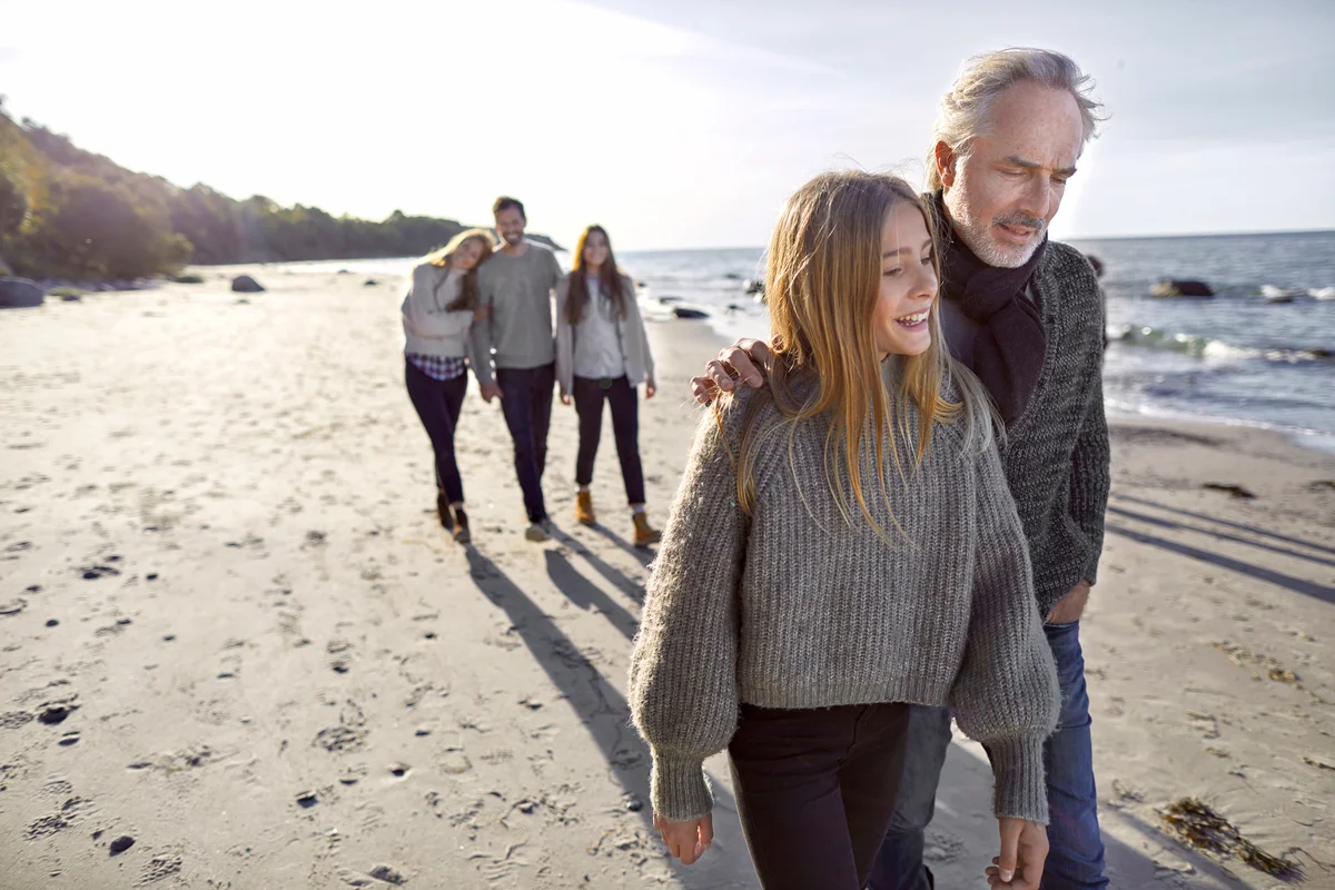 Step-dad and daughter strolling on the beach with family in background