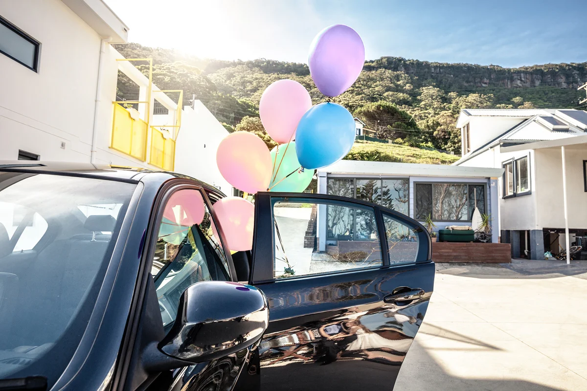Woman holding baby colored balloons out of a car