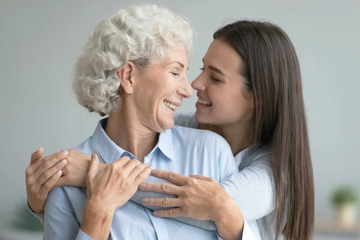 Smiling adult daughter and senior mother hug at home