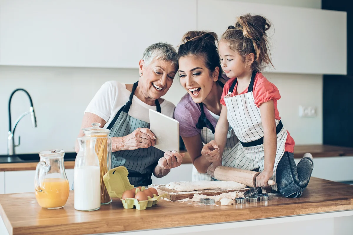 Different generations of women with digital tablet preparing cookies together