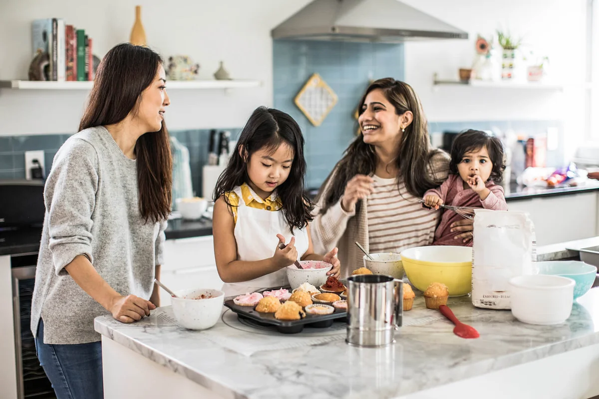 2 mothers with children makings cupcakes in kitchen