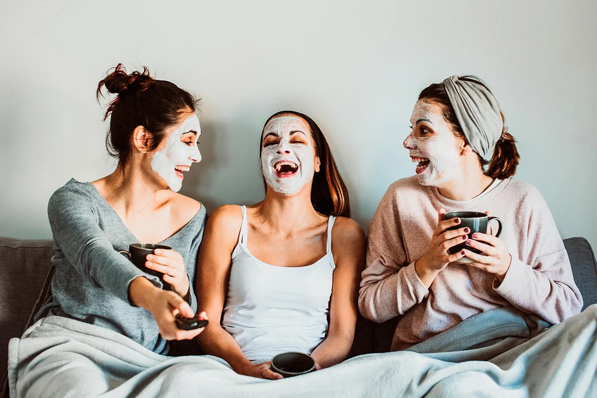 Cheerful Women With Facial Mask Sitting On Sofa At Home