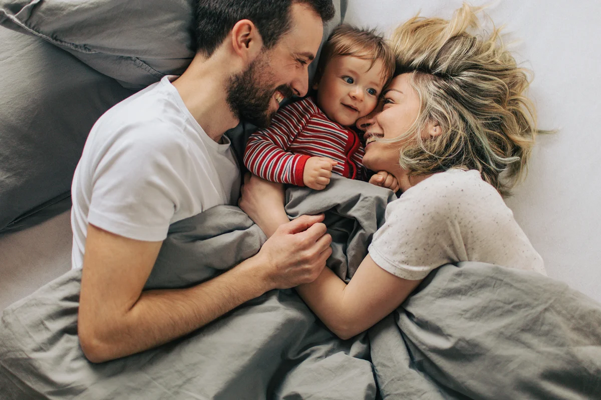 Young parents enjoying morning routine in a cosy bed with their baby boy