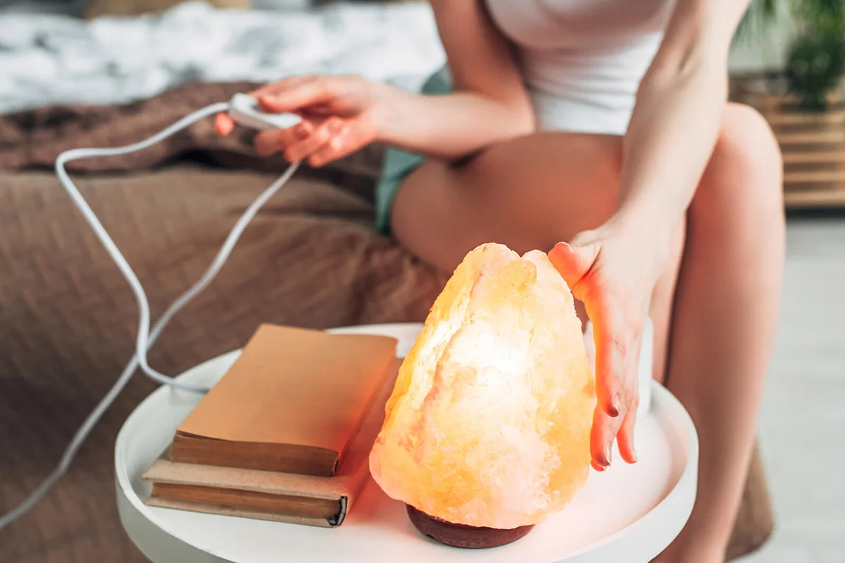 young woman switching Himalayan salt lamp in bedroom with book