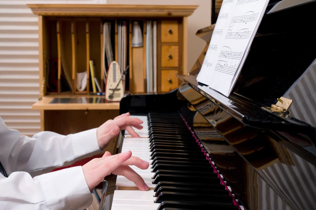 Kid playing the piano with a music sheet cabinet in the back