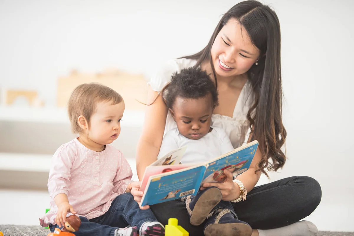 woman reads a picture book to the babies on her lap