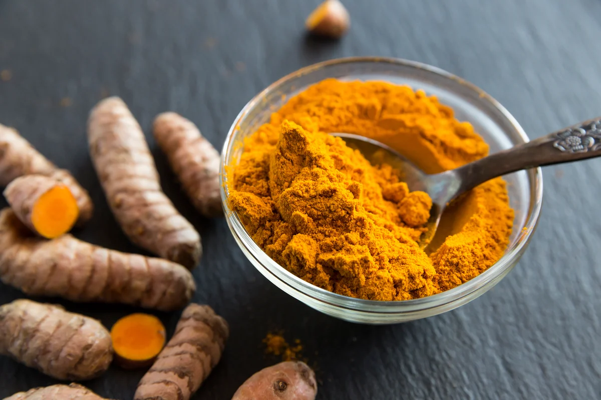 Glass bowl of curcuma powder and fresh organic curcuma on slate