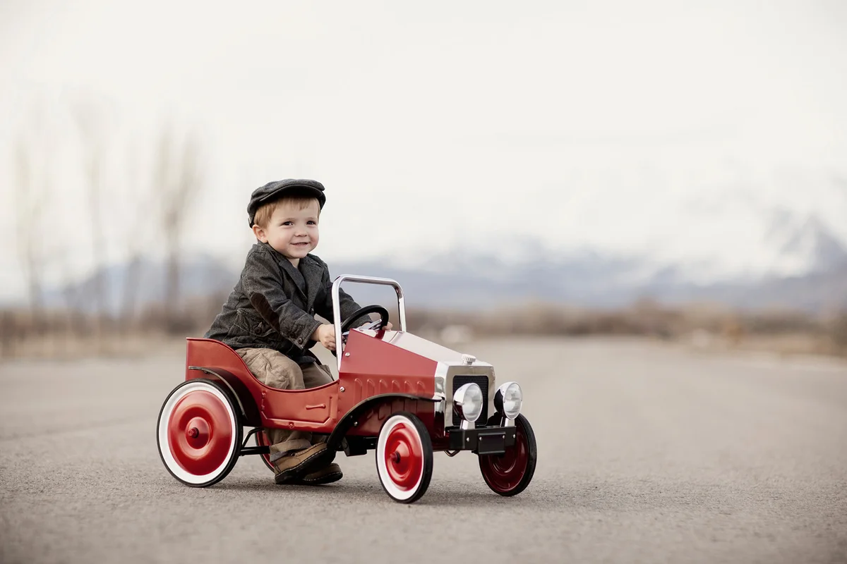 A young boy driver is out for a drive in his pedal car.