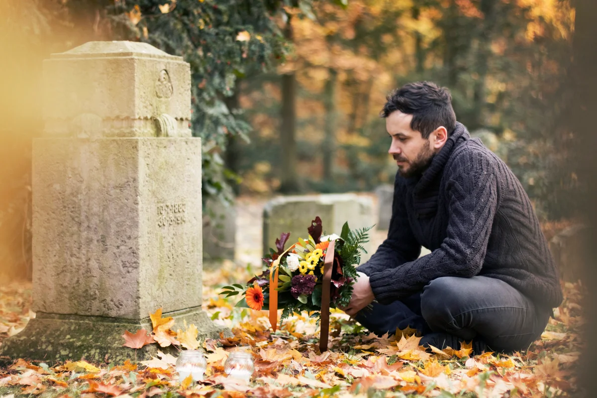 Mid adult man with flowers and candles visiting graves at the cemetery