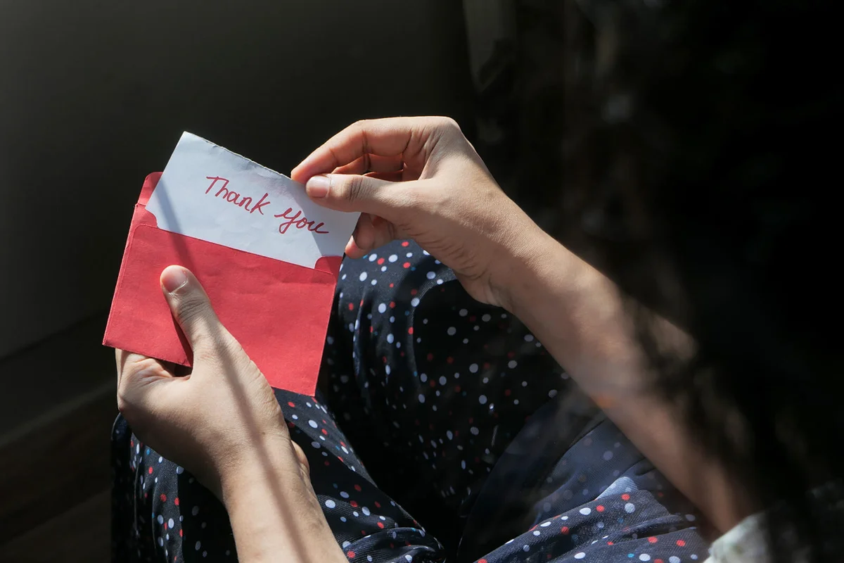 women's hand holding thank you note