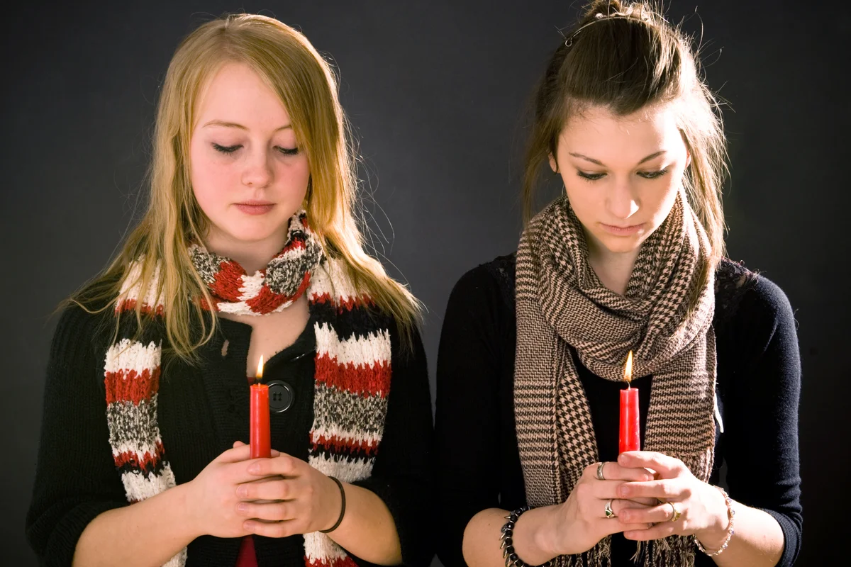 Two young women look down at burning candles and remember during a moment of silence