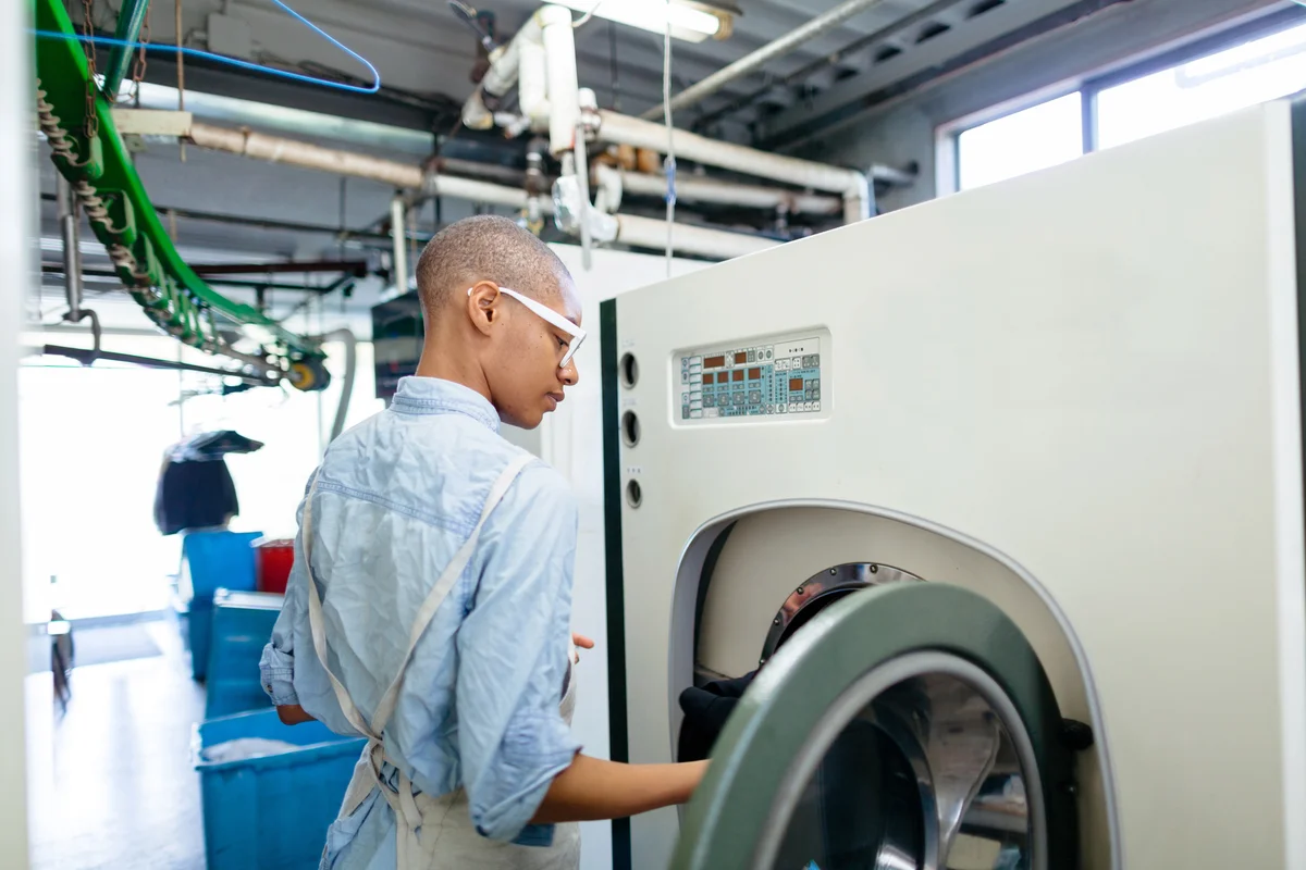 Young woman putting clothes into dry cleaning machine