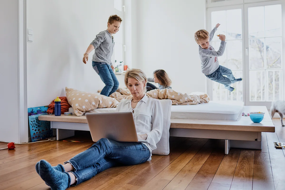 Mother using laptop at home with children romping around in background