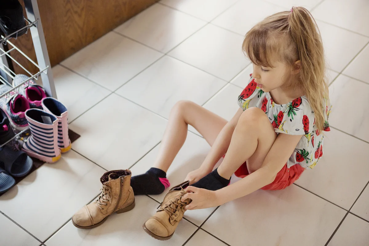 Child putting lace-up boots on herself