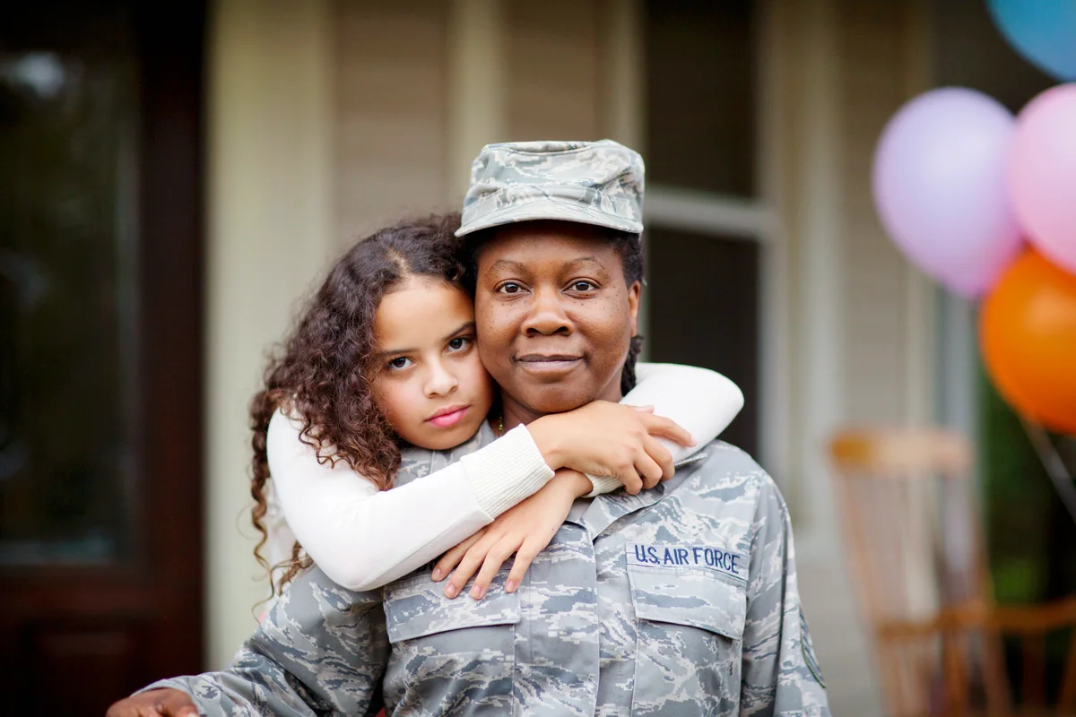 Daughter embracing her soldier mom against house