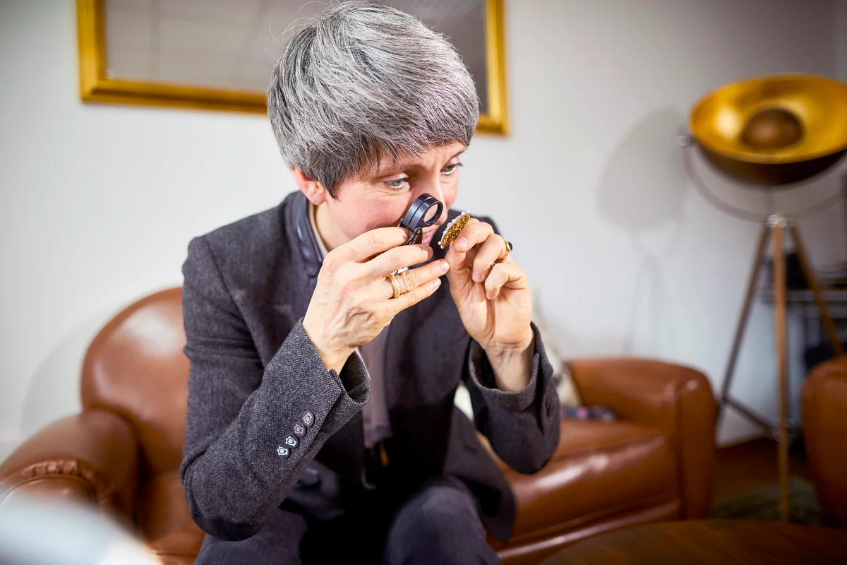 Goldsmith examining piece of jewelry with a magnifying glass