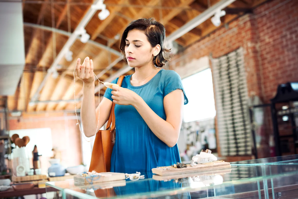 Young woman standing in a shop, looking at a necklace