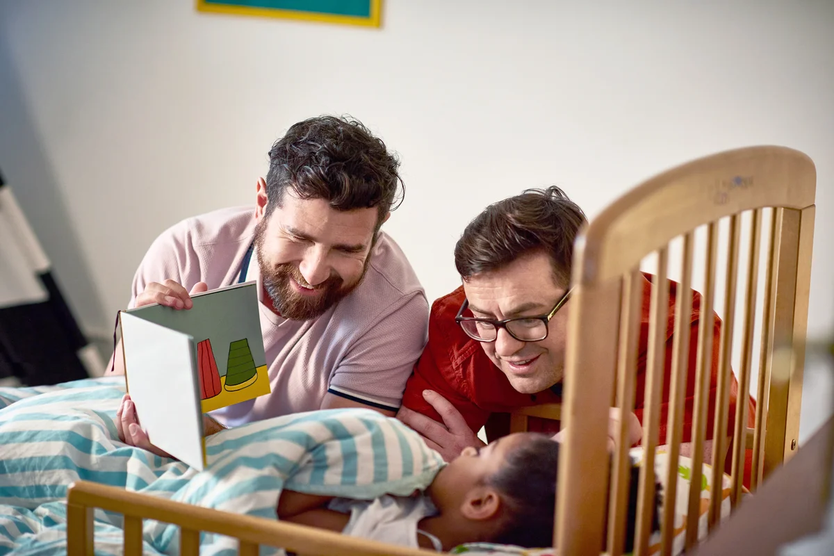 Adoptive fathers reading bedtime story to daughter