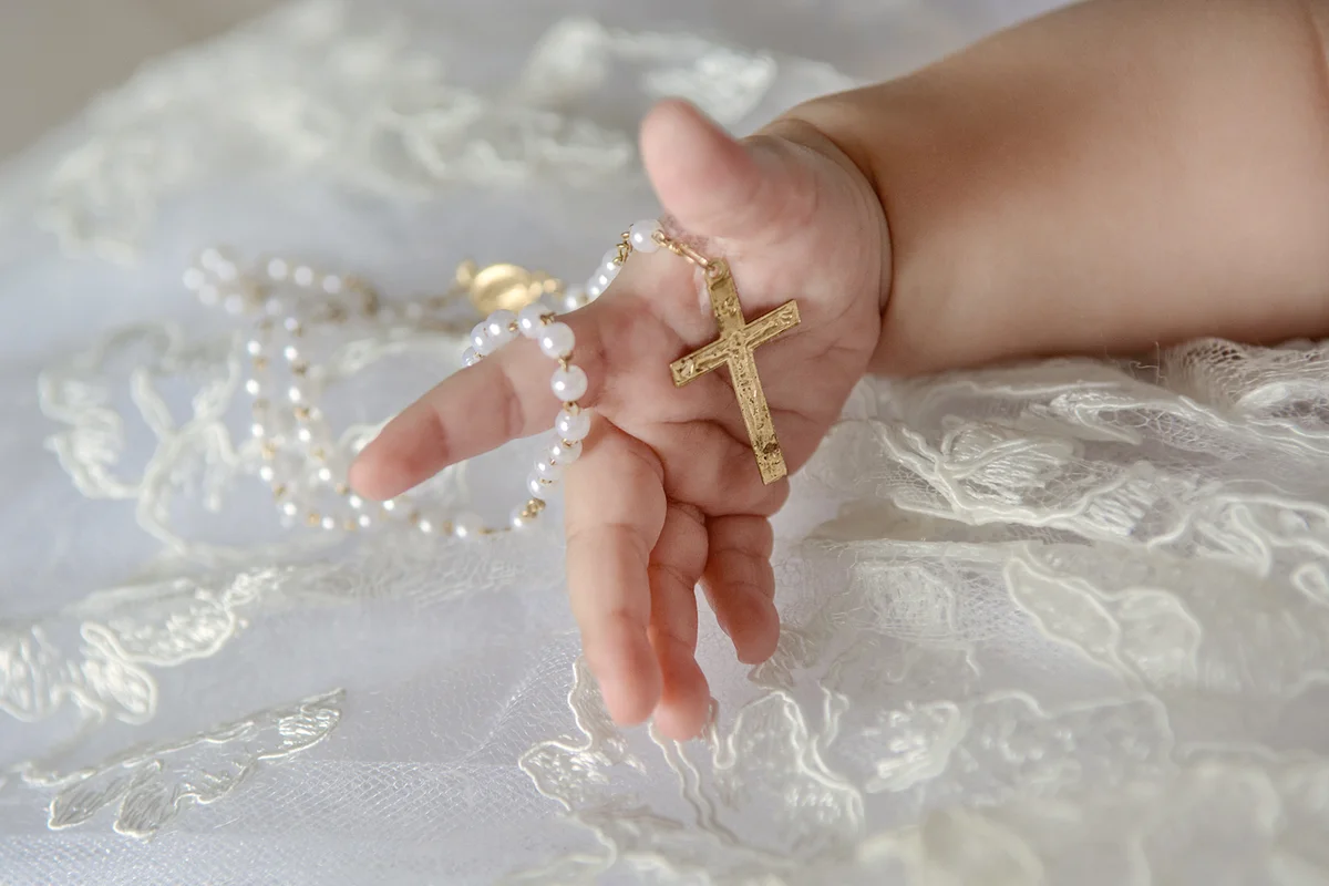 Child's hand with a crucifix on a white cloth background.