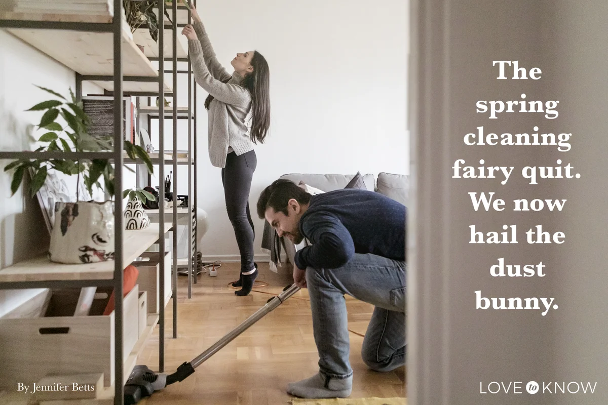 Man vacuuming floor while woman cleaning shelf at home