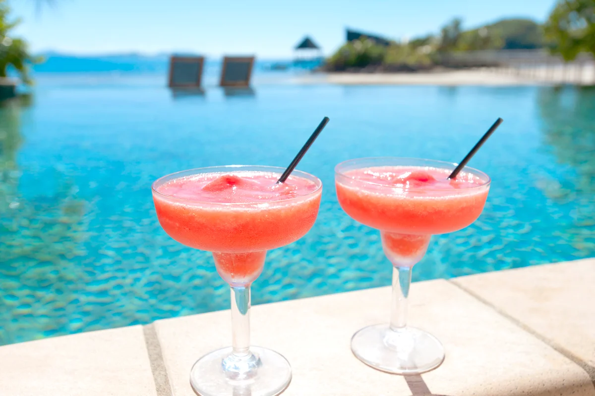 Two strawberry daiquiris beside a resort swimming pool