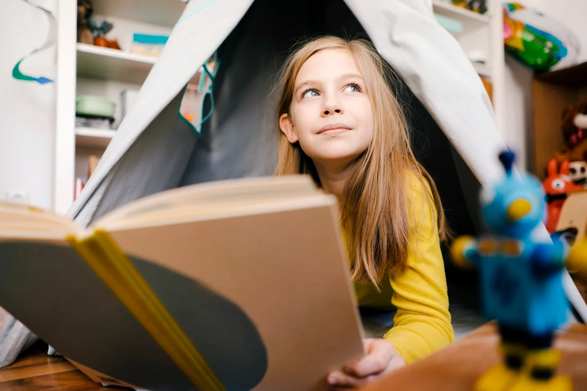 Girl at home reading book in children's room inside tent
