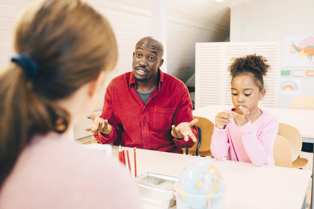 Surprised man sitting with son talking to teacher at classroom