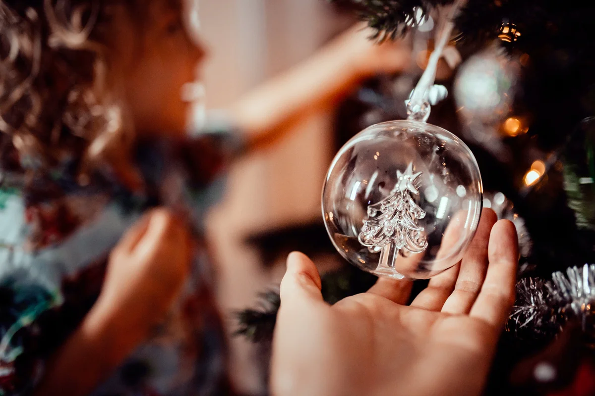 Little girl admires the Christmas tree ornaments with Mum