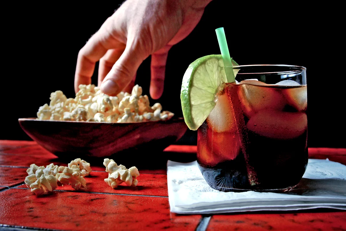 Man's hand in popcorn bowl and charro negro in glass on bar counter