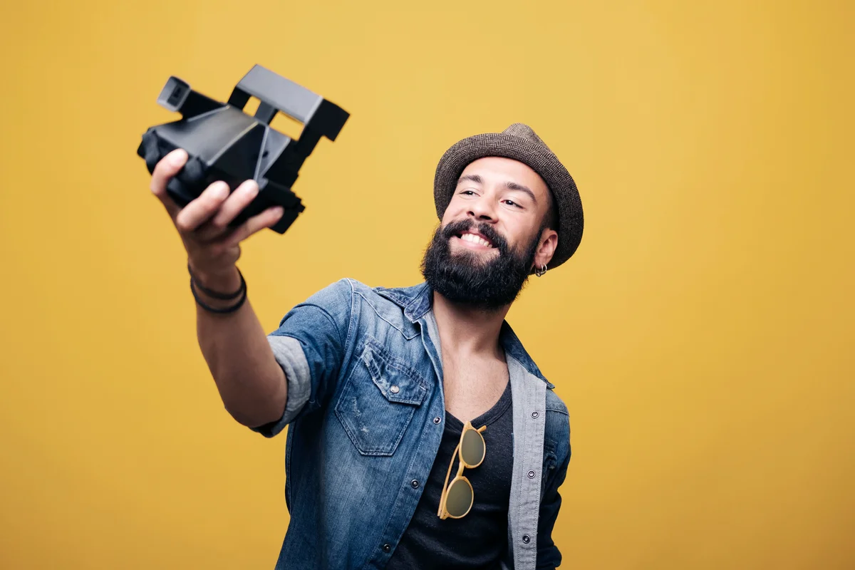 Bearded young man in studio taking selfie with instant camera