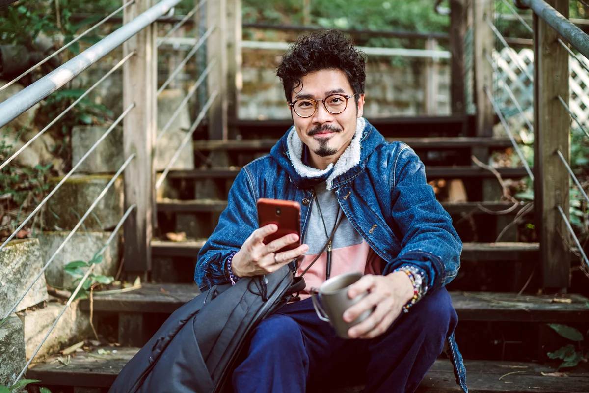 Young man smiling joyfully at camera while using smartphone in country side