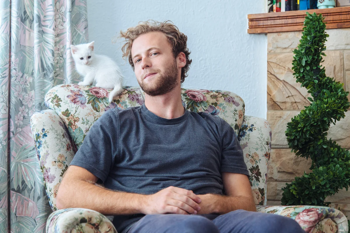 Young man sitting at home with small white kitten