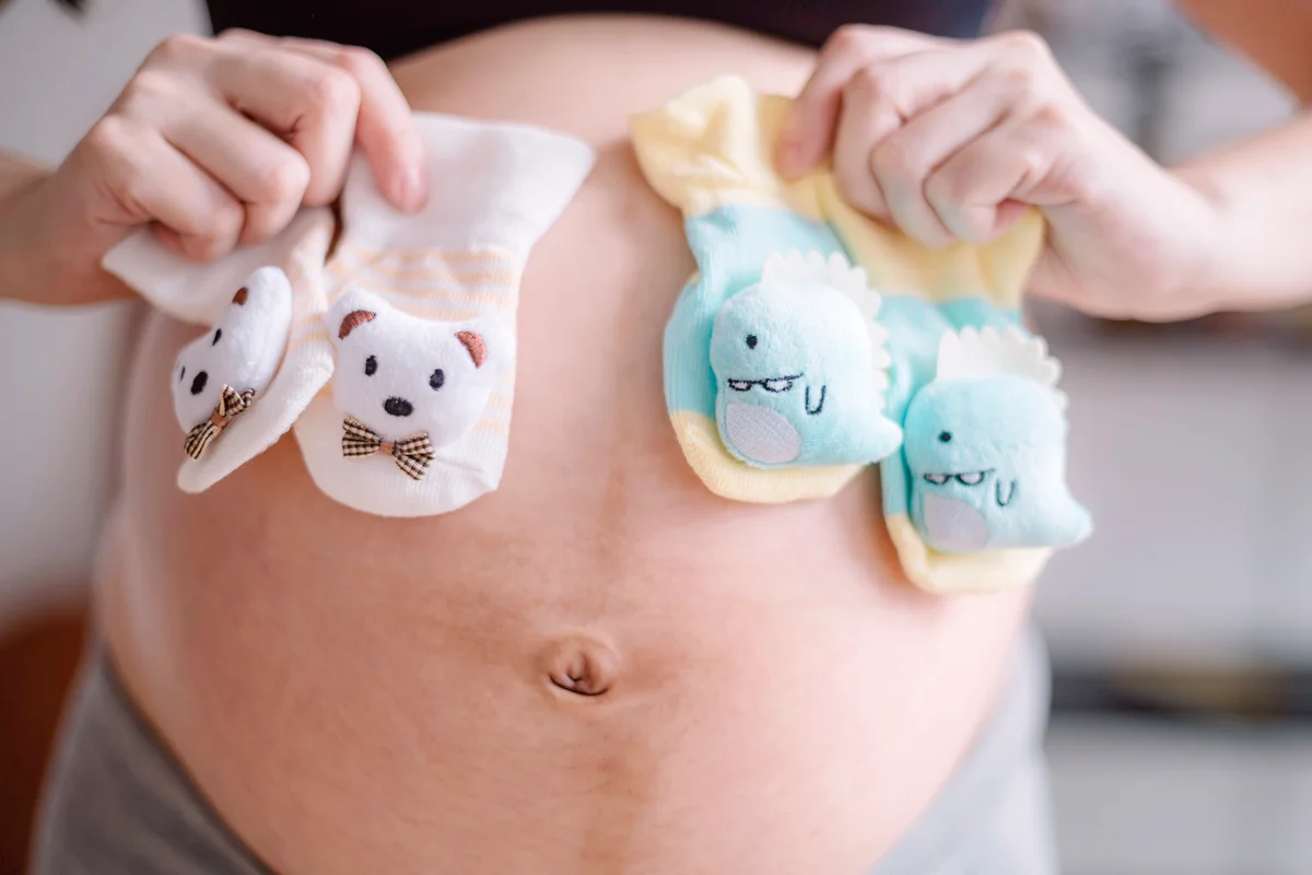 Pregnant lady holding 2 pairs of baby booties in front of her belly
