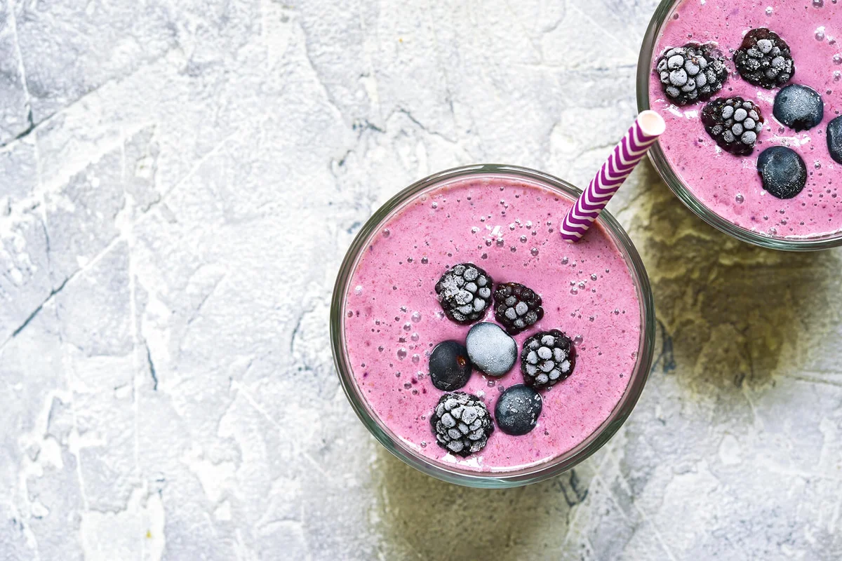 Two portions of berry smoothies in a glasses with paper straws
