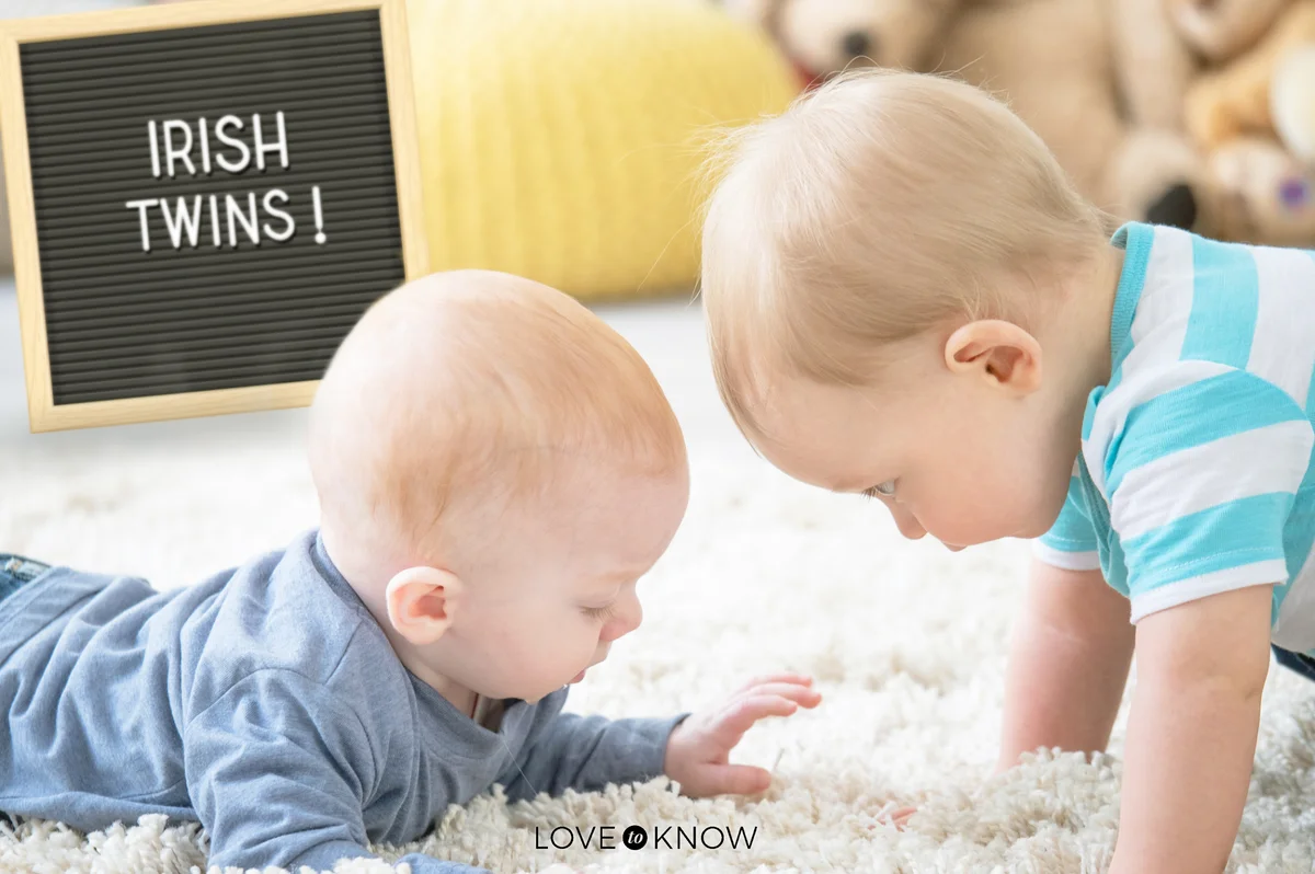 Two babies brothers lying down on a white carpet