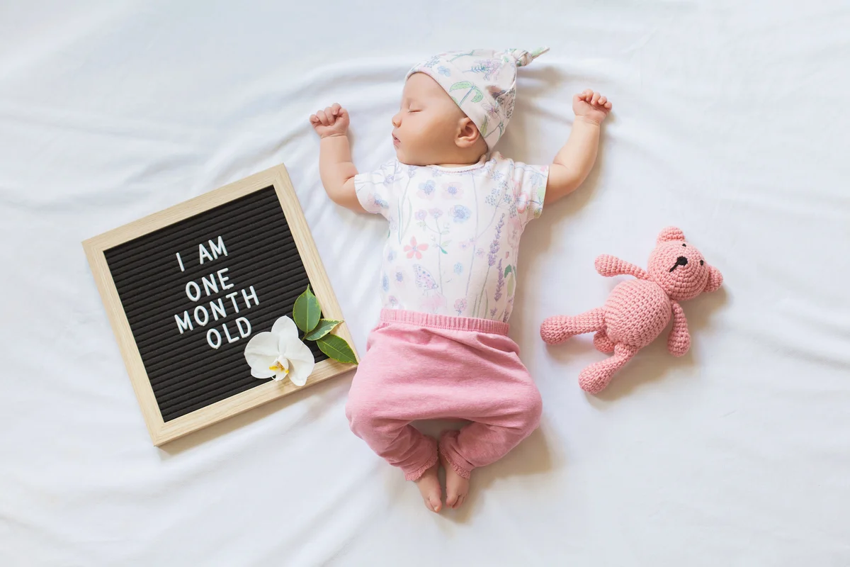 Sleeping one month old newborn baby girl laying between letter board and teddy bear