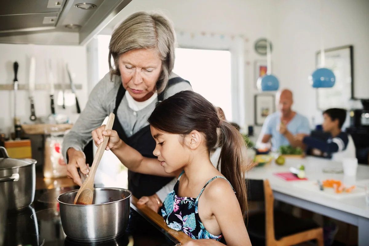 Grandmother looking at girl cooking at kitchen counter