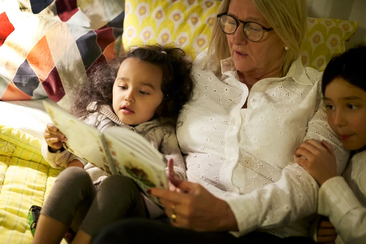 Grandmother reading book to granddaughters while lying on bed at home