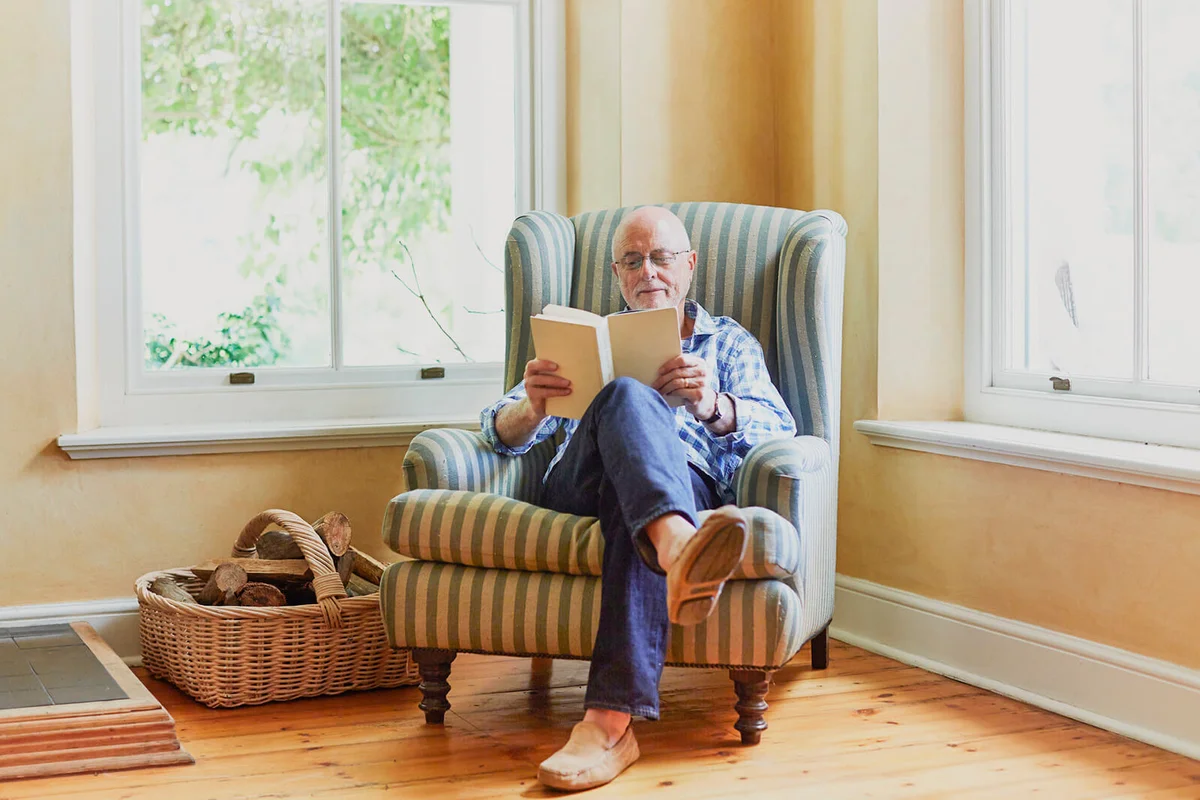 Full length of senior man reading book while relaxing on chair at home