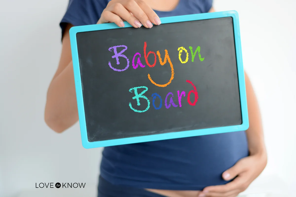 Pregnant woman holds baby on board colored text over belly