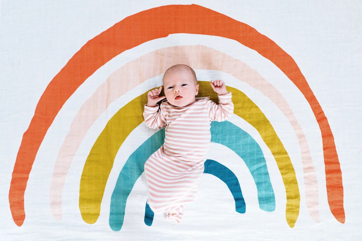 A newborn baby girl lying on a rainbow painted blanket